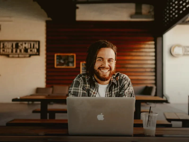 A freelancer smiling at his laptop in a café