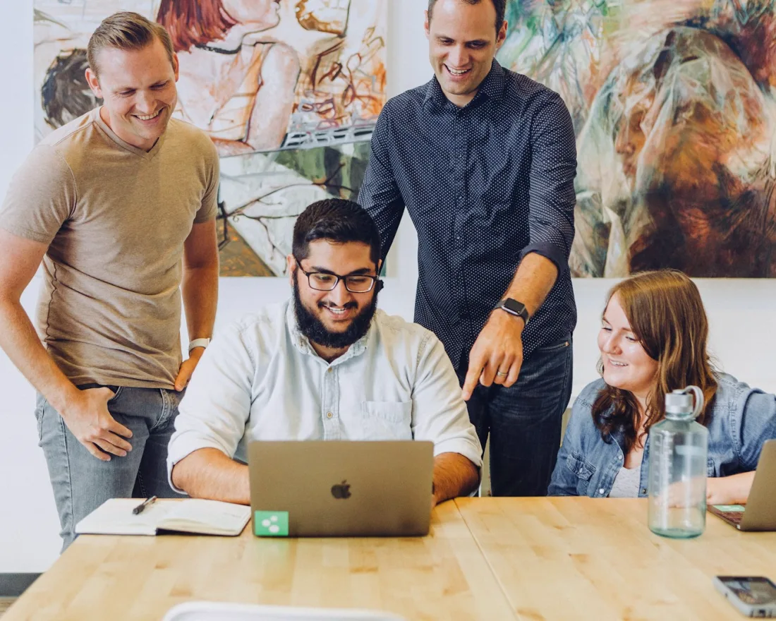 A small web team smiling as they review a website on a laptop